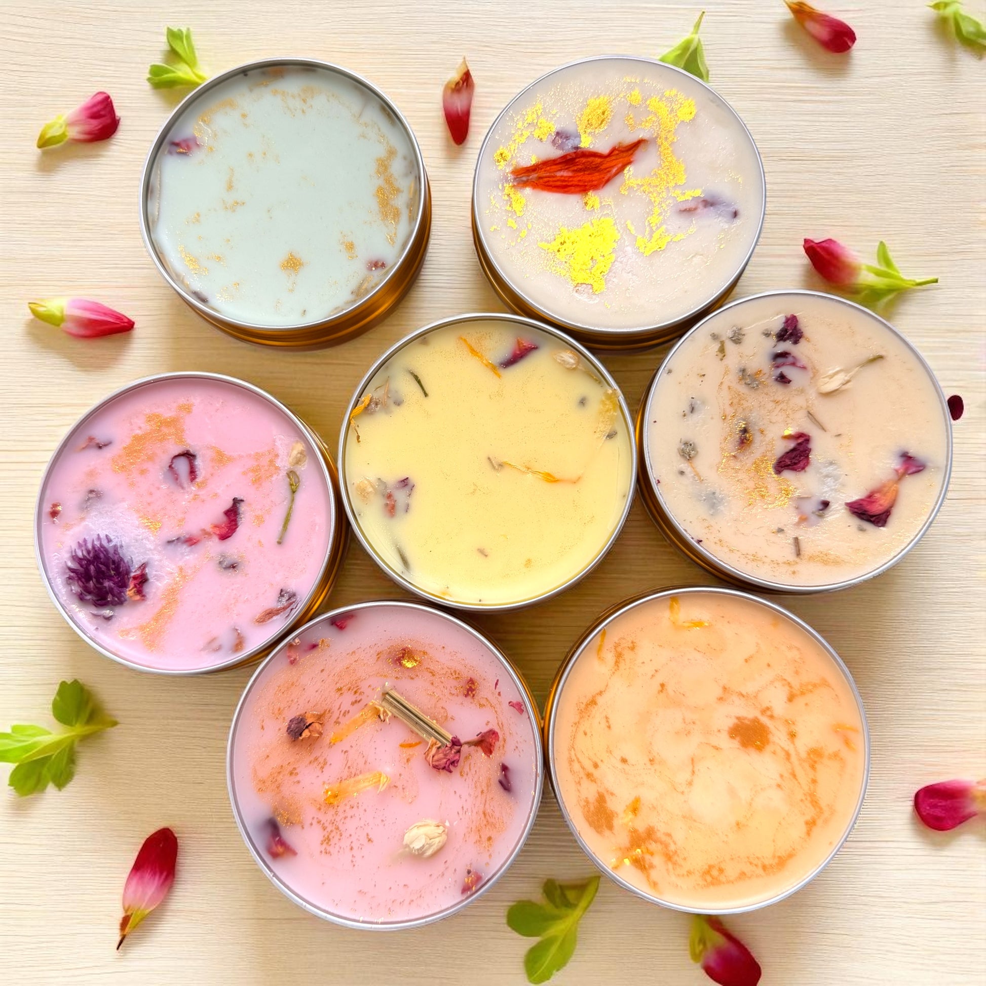 Assorted candles in metal tins on a light wooden surface with flowers.