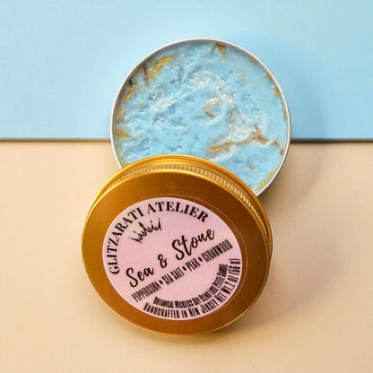 Open container of sea salt scrub with decorative lid on a beige surface