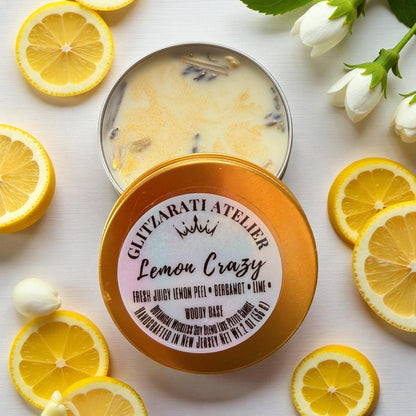 Candle in a tin labeled 'Lemon Crazy' by GLITYZARATI ATELIER surrounded by lemon slices on a light background.