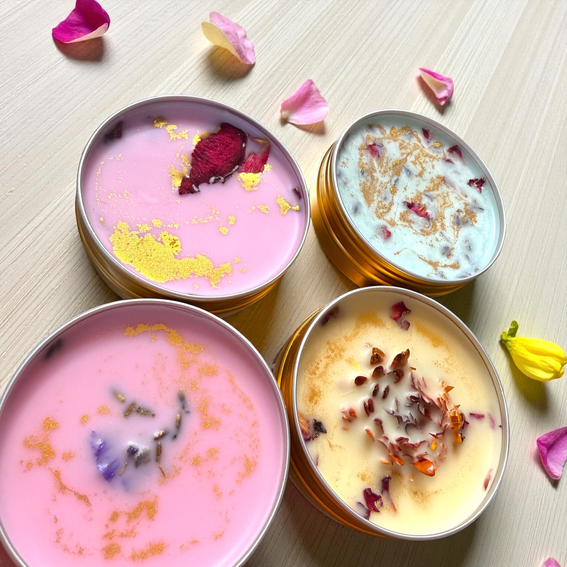 Four small containers of bath salts with decorative elements on a light wooden surface.