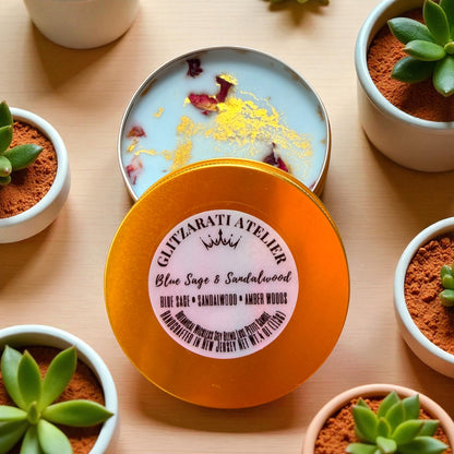 Open container of Blue Sage & Sandalwood incense with decorative elements on a wooden surface surrounded by small potted plants.