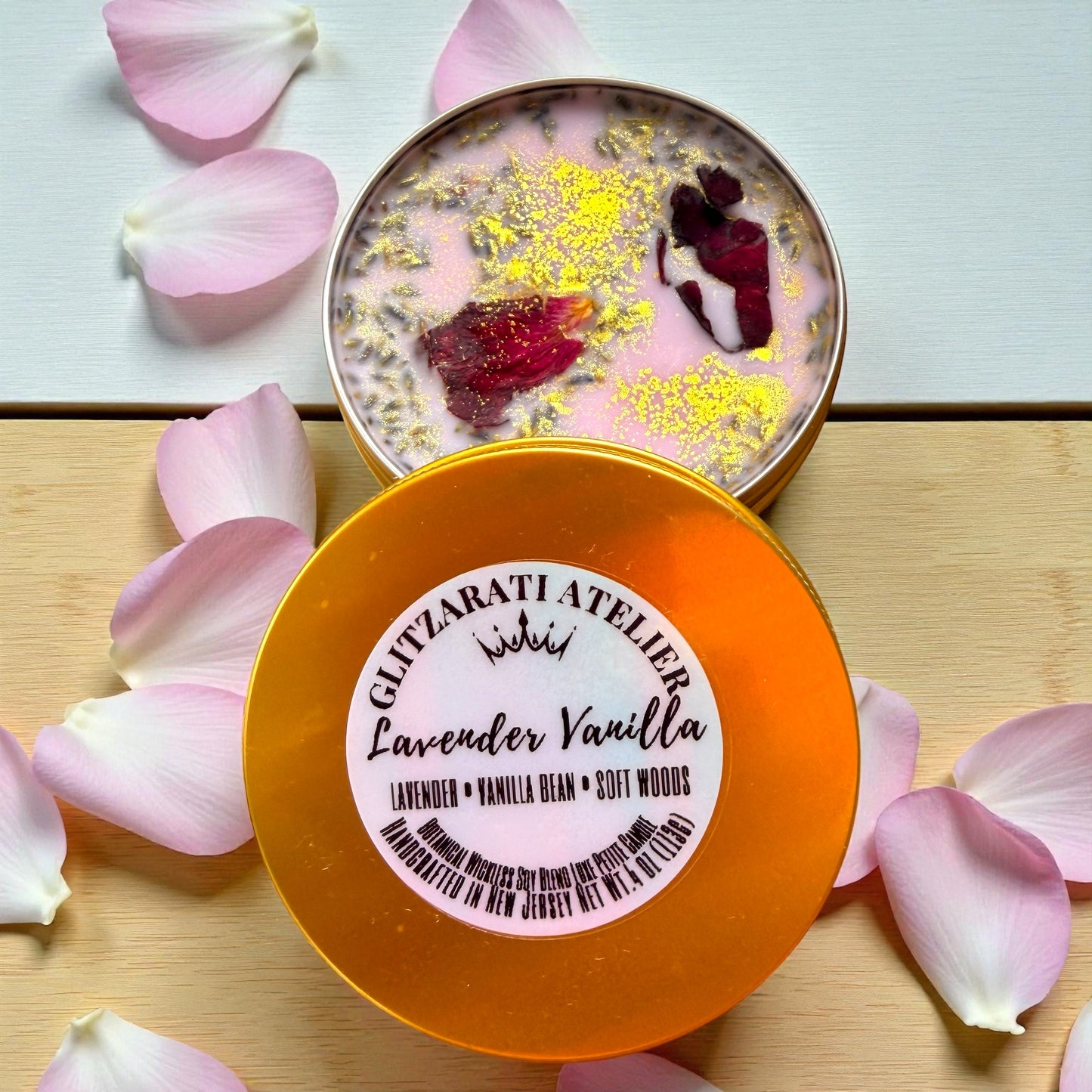 Decorative container with 'Glycyrrhizi Atelier' label surrounded by pink petals on a light wooden surface.