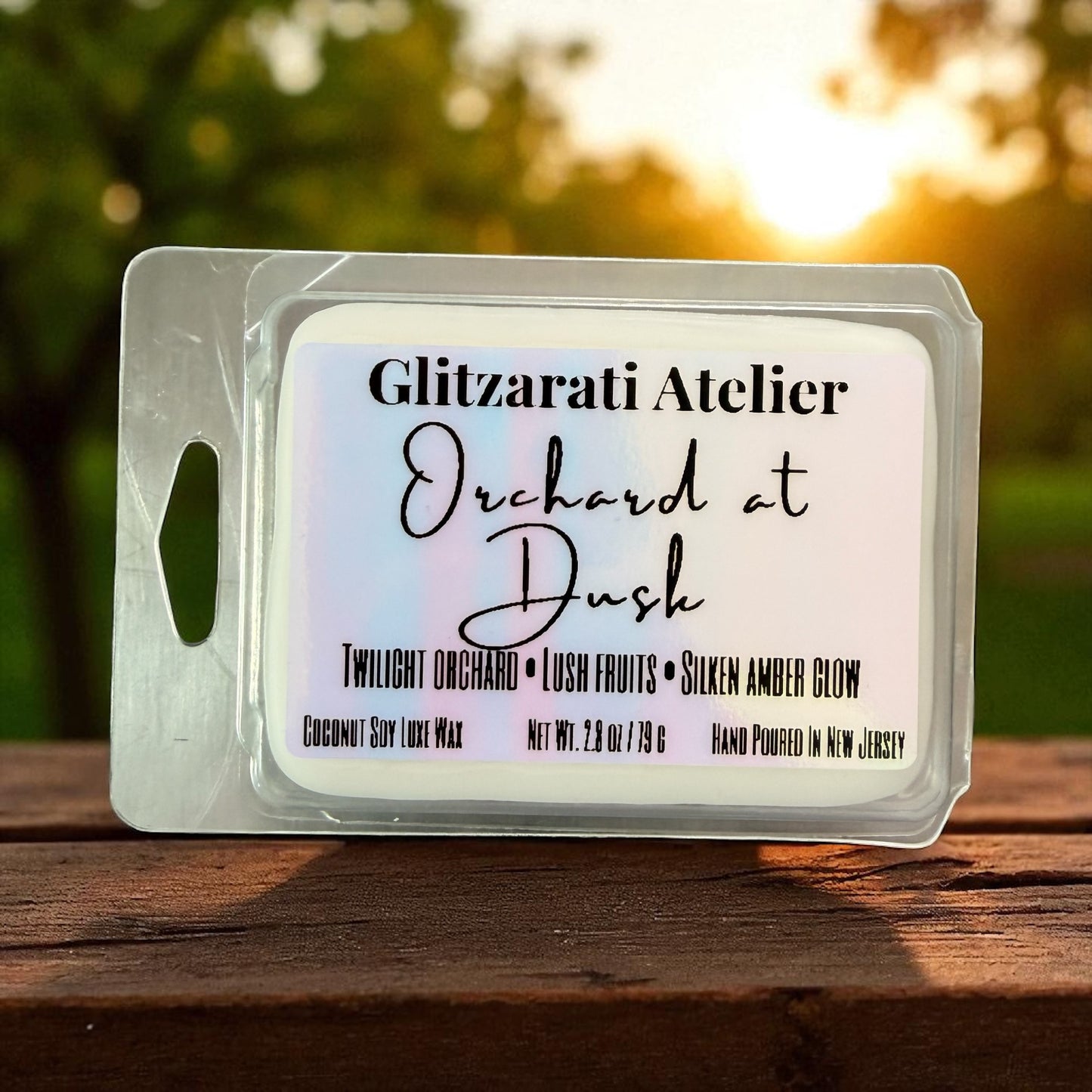 Wax melt packaging with 'Glitzerati Atelier' branding on a wooden surface with a sunset background.
