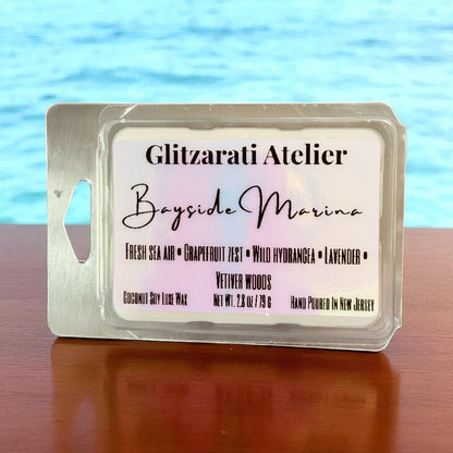Wax melt packaging with 'Glitzarati Atelier' branding against a blue water background
