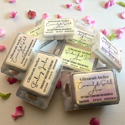 Packaged wax melts from Glitzarati Atelier on a light surface with pink flower petals.