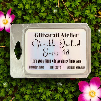 Wax melt package labeled 'Vanilla Orchid Oasis 48' by Glitzerati Atelier on a green leaf background with flowers.